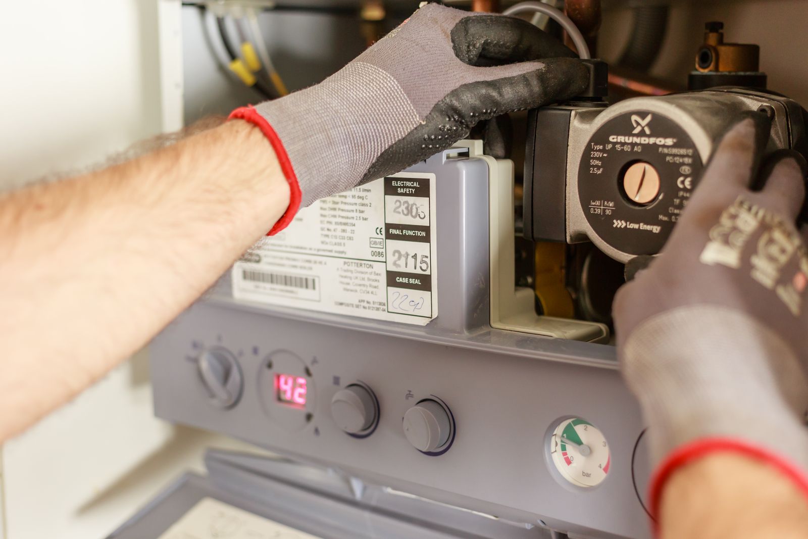 Technician's gloved hands servicing the internal components of a home heating boiler