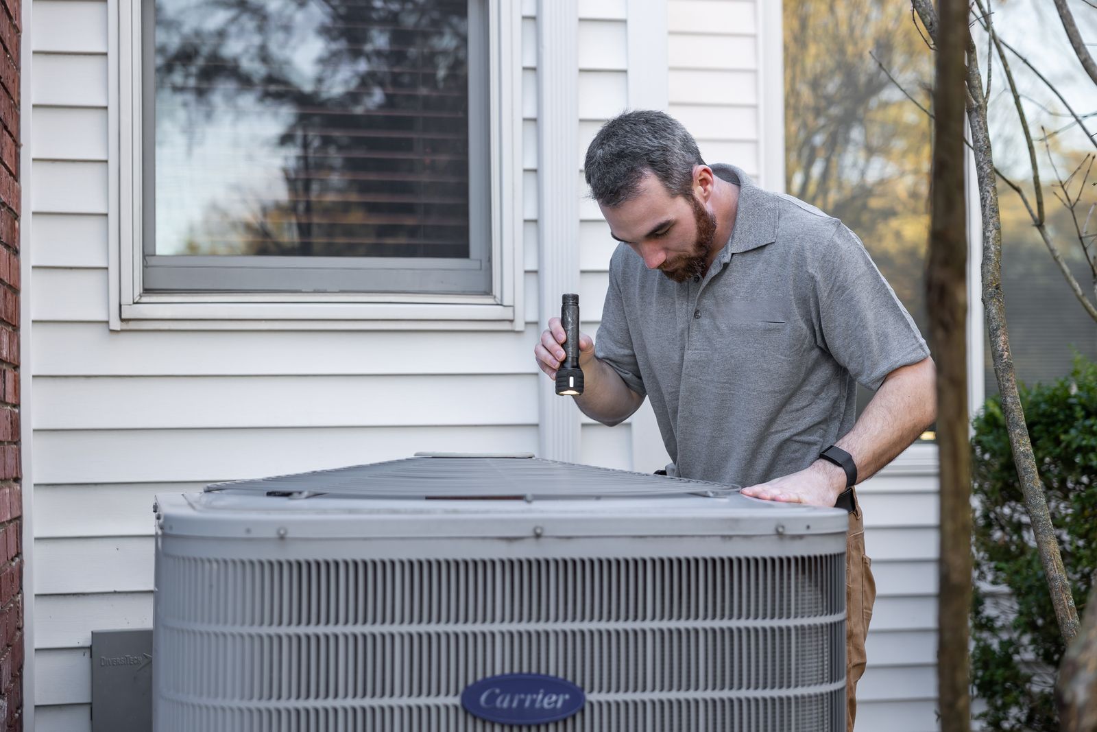 HVAC technician inspecting an outdoor air conditioning unit beside a home during a maintenance check